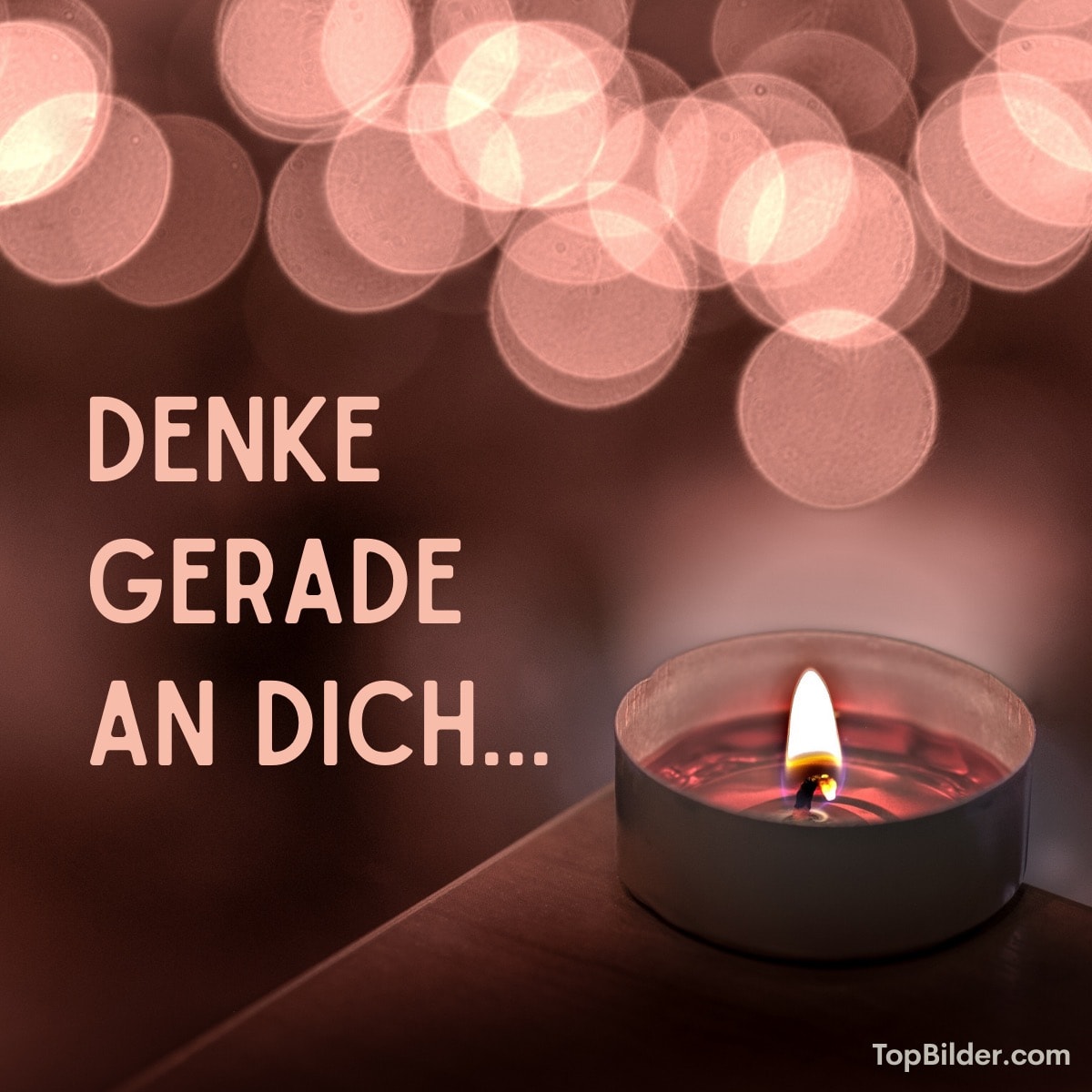 Eine Kerze mit dem Text „DENKE GERADE AN DICH...“ und unscharfen Lichtern im Hintergrund